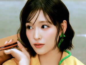 石井蘭(RAN) 黄色いシャツを着てどこかを見つめている